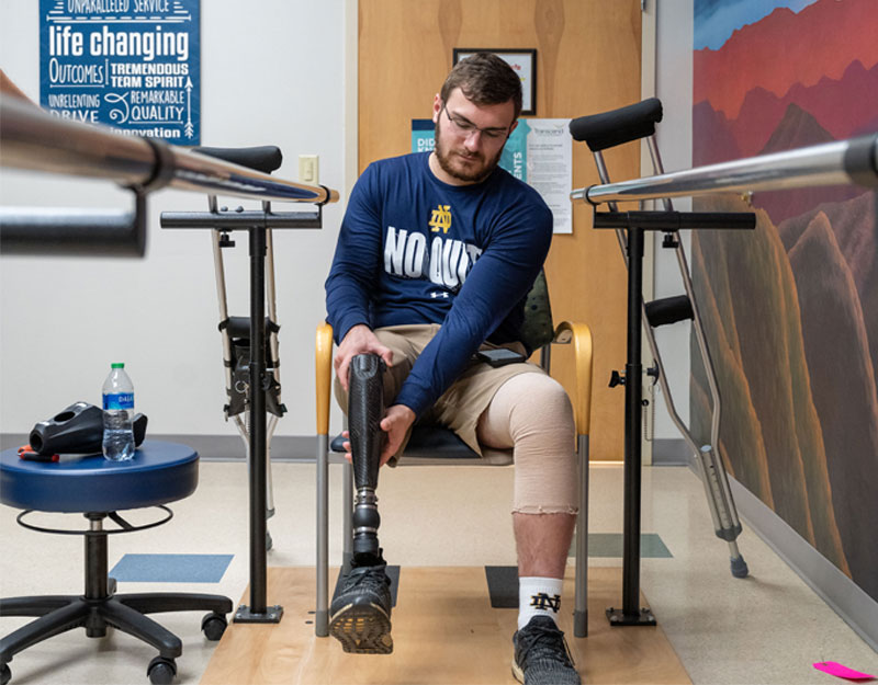 Andrew sits in a chair and tries his prosthetic leg on for the first time.