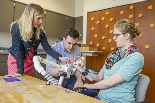 A male and a female physical therapist help a woman work a prosthetic pvc pipe system.