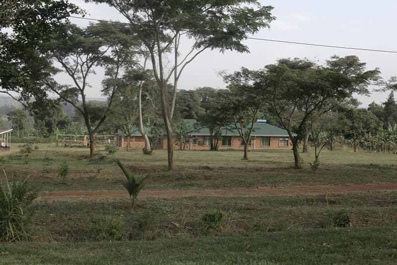 A one-story brick building surrounded by trees. A dirt path in the forground.