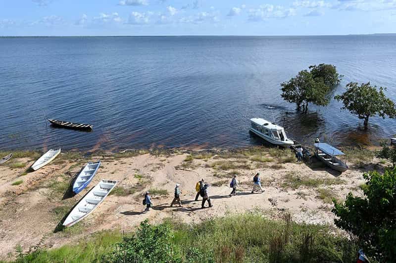 A group of people walk on a beach where multiple canoes and boats are docked.