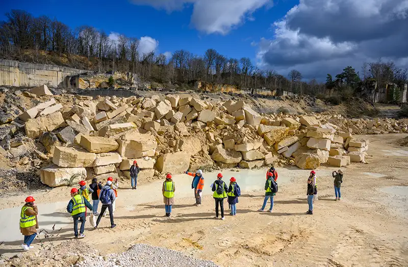Wide angle view of many Notre Dame architecture students standing at the base of a pile of cut stones at the quarry.
