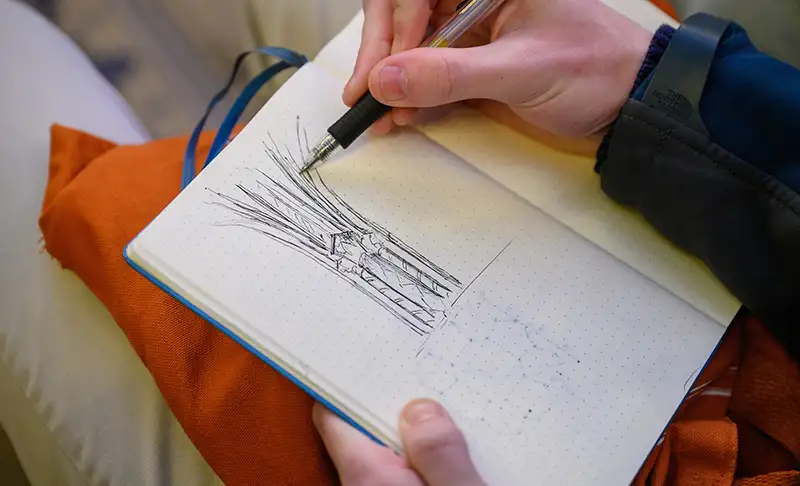 Seated student sketching a pillar in his sketchbook.