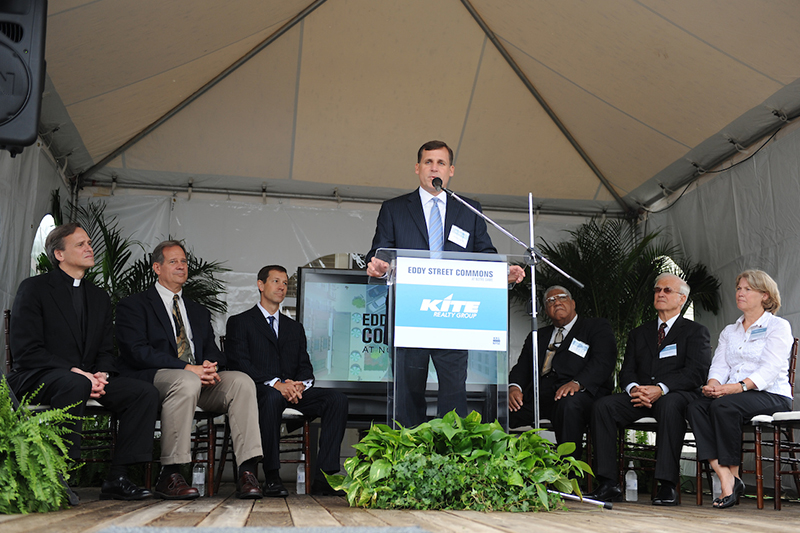 Kite Realty Group's COO stands at a podium with representatives from Notre Dame and Kite Realty seated behind him.