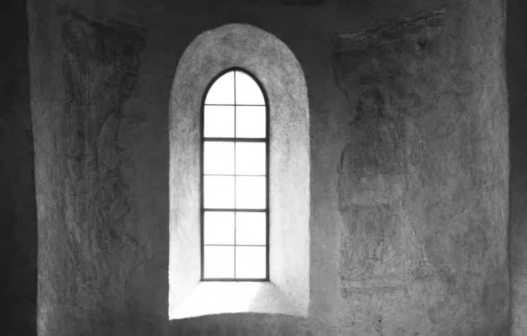 A black and white photo of a simple church window surrounded by stone.