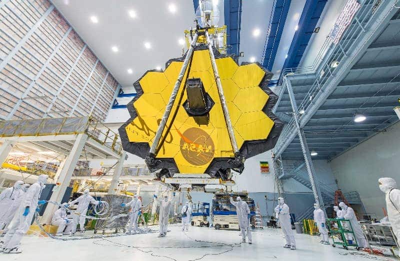 NASA's James Webb Space Telescope, 8 gold-plated hexagonal segments that unfold like a 21-foot blooming flower, is lifted over a team of people.