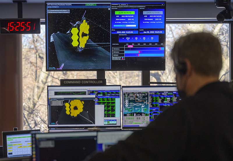 A blurred figure in the foreground keeps watch over multiple monitors that display the Webb telescopes progress in space.