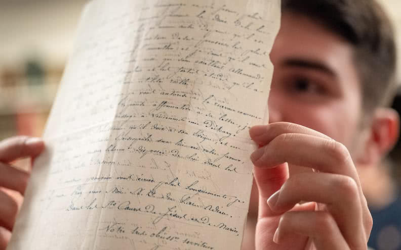 A student holds up a piece of paper with calligraphic writing on both sides of it up to the light.