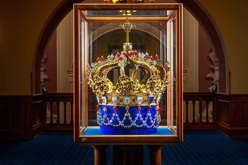 An ornate gold crown sits in a clear glass box.