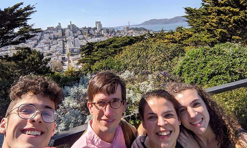 Four people take a selfie together overlooking trees and city in the background.