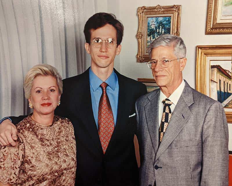 Schnell stands between a man and a woman, with his arms around their shoulders.