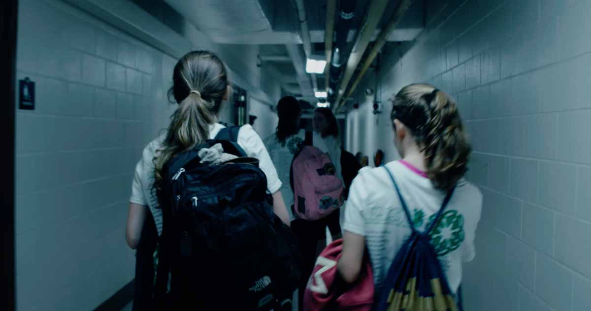 A view from behind the dancers walking down a cinder-block hallway