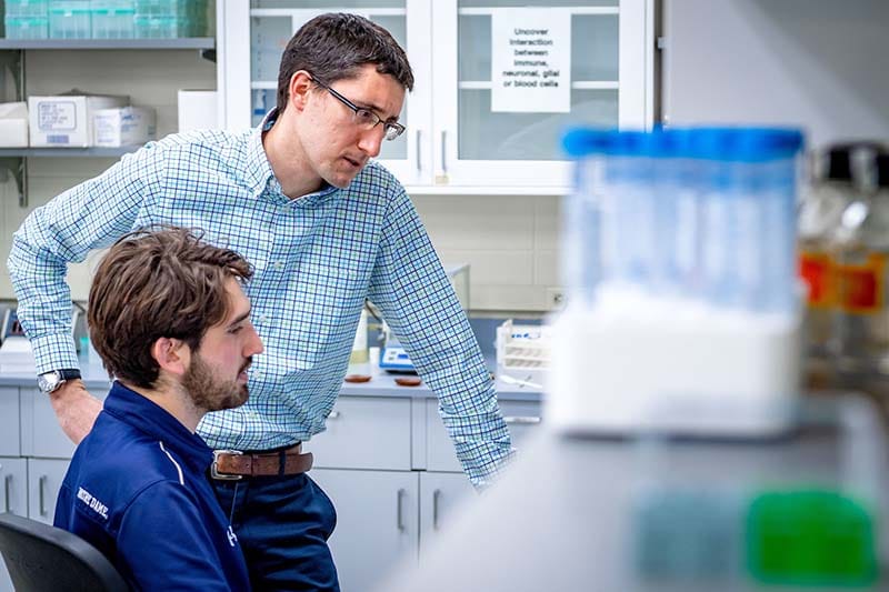 Two men in a lab study an image on a computer screen.