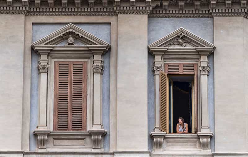 A woman looks outside her balcony window.