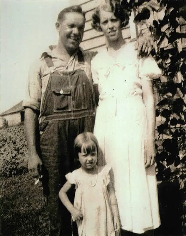 An old black and white photo from 1934 showing a man in overalls and a woman in a dress with a child standing in front.