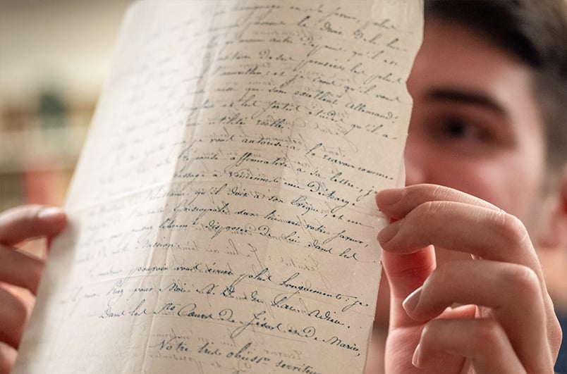 A student holds up a piece of paper with calligraphic writing on both sides of it up to the light.