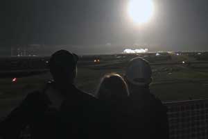 In the foreground, three people hug looking at a spaceship launch.