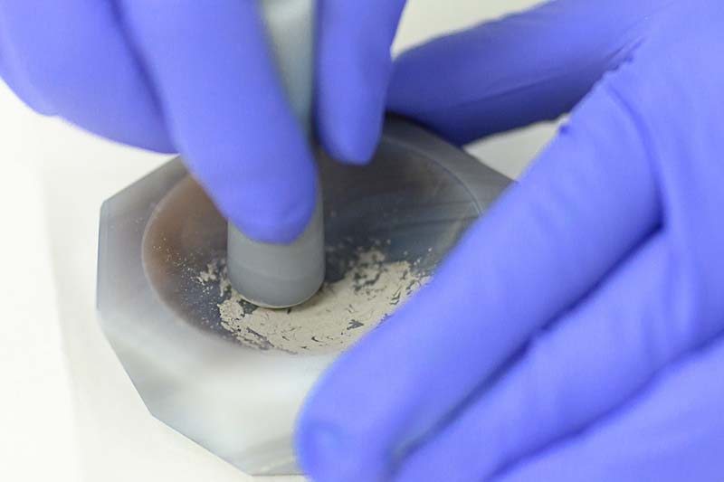 A close up shot of hands wearing rubber gloves grinding samples of lunar rock.