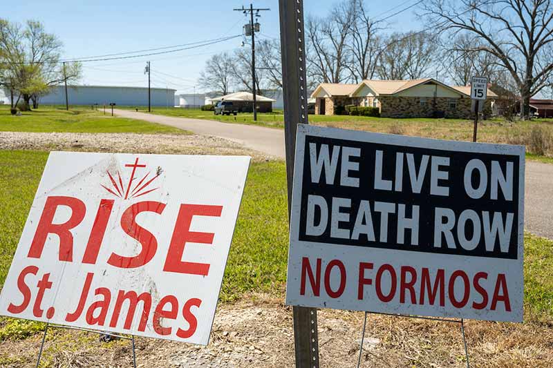 Two yard signs in a neighboorhood that say 'RISE St. James' and 'We live on death row - No Formosa'.