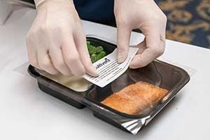 Gloved hands place a label on a package of food.