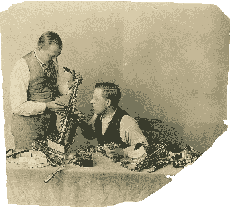 Two white men, one sitting and one standing both look at a saxophone. 