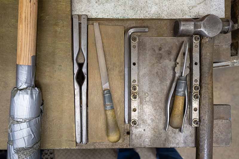From above, tools such as pliers and hammers lay on top of a table.