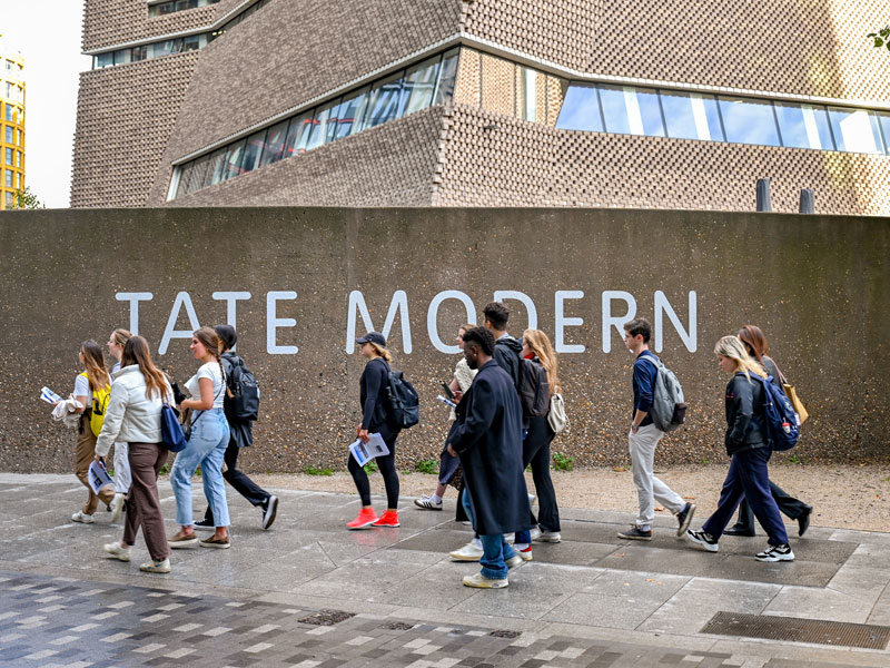 A group of students stand in front of the brick wall of the Tate Modern.