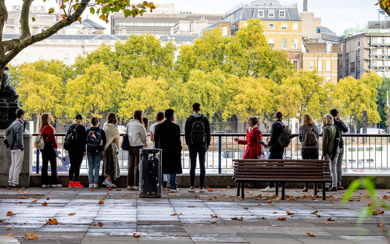 A group of people stand at the fence along the River Thames in London.