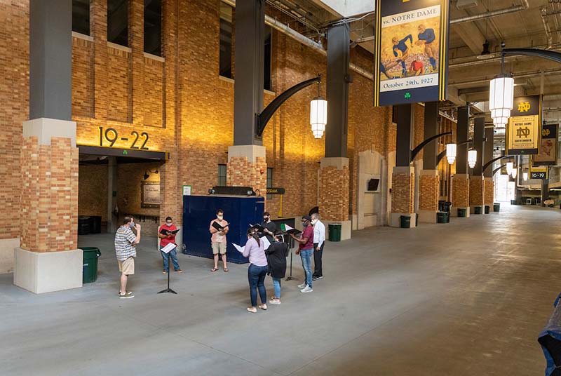 A group of students sing in the concourse, with football signage around them.