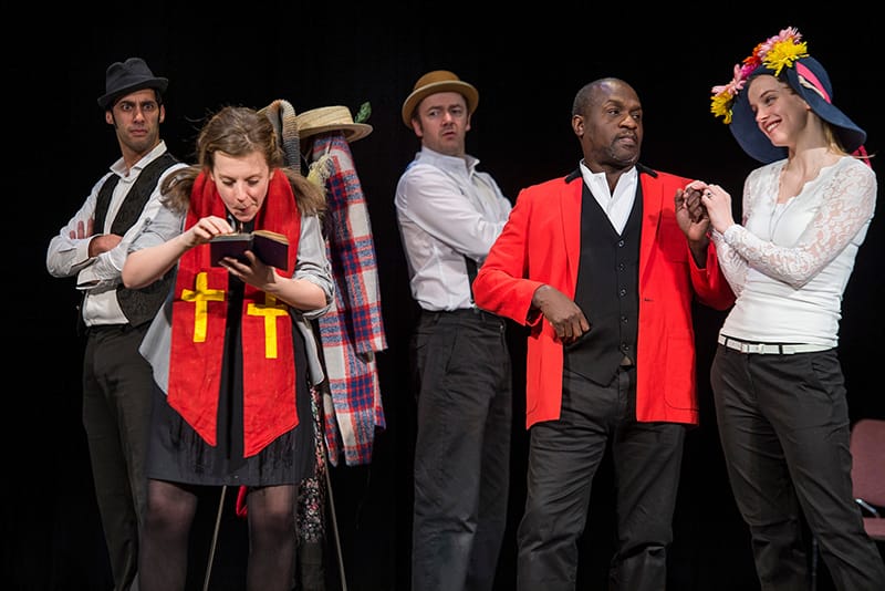 Students performing As You Like It on stage wearing a variety of colorful outfits