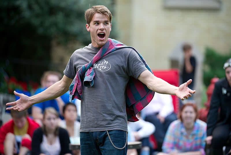 A young man performing at Notre Dame Shakespeare Festival while wearing a plaid shirt as a cape