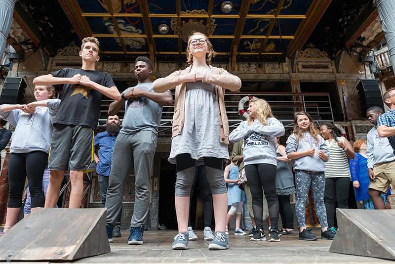 Over a dozen students from Robinson Community Learning Center in London standing on a stage with their fists touching in front of their chests