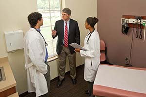 A professor works with medical students in a patient room.