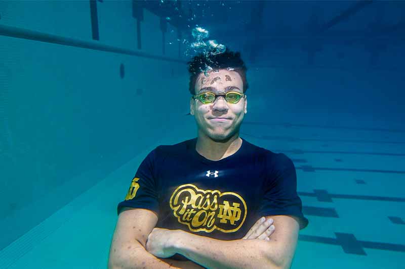 A college student wearing goggles crosses his arms and floats under water.