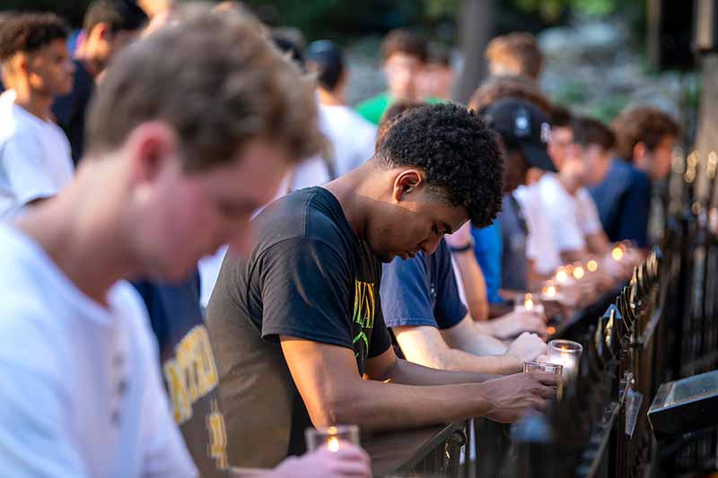 A group of students kneel and pray while holding lit candles.