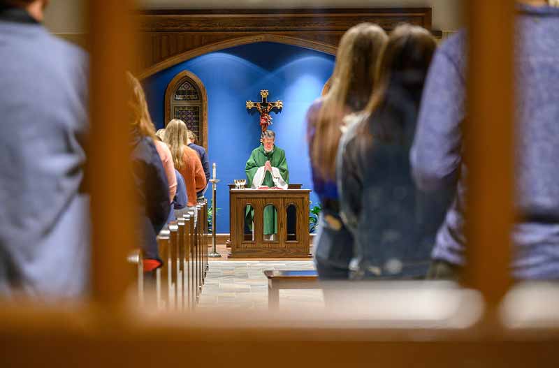 Rector Rev. Paul Doyle, C.S.C., a priest, stands in front of a congregation and prays.