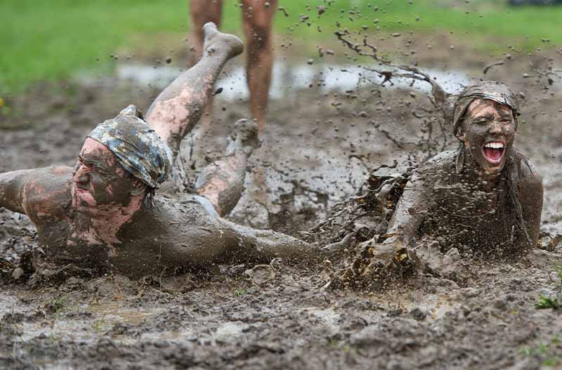 Two people covered head to toe in mud slide slide on their stomachs in mud.