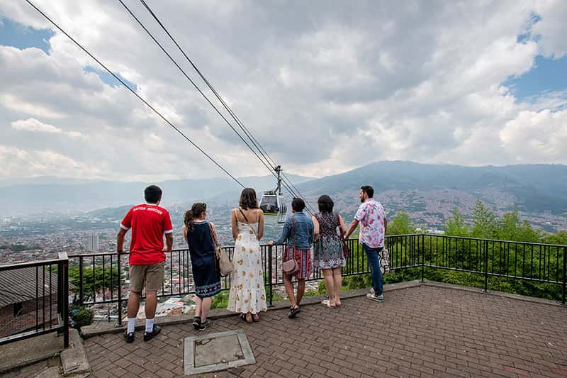 Six people lean over a railing overlooking Medellín cable cars.