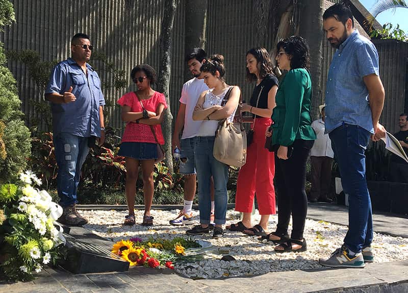 People stand around and listen to a tour guide at Pablo Escobar's grave.