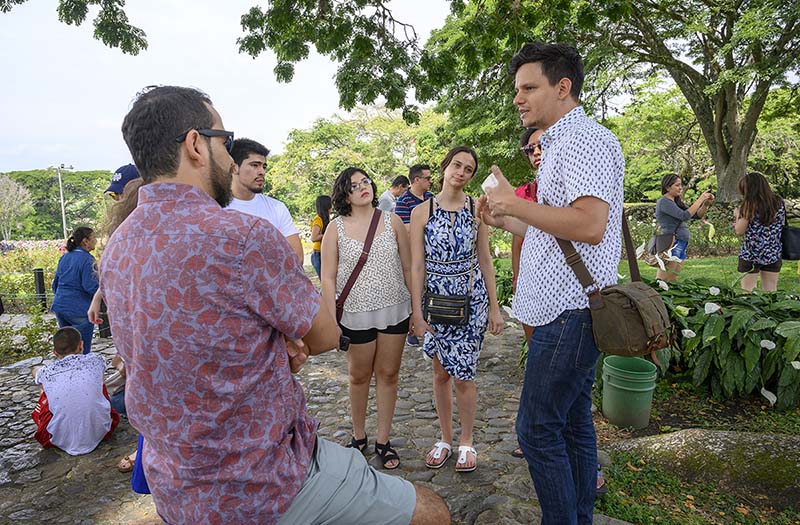 Outside surrounded by lush greenery, a man speaks to a group of students.