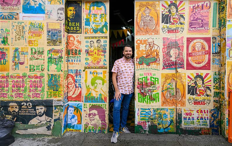A man stands against a colorful wall of murals.
