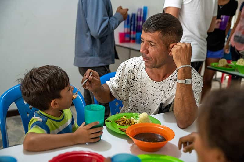 A man feeds his young son with a spoon.