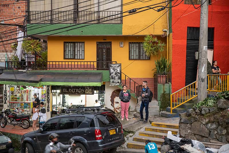 Colorful buildings on a street with Pablo Escobar themed signs advertising souvenirs and other items.
