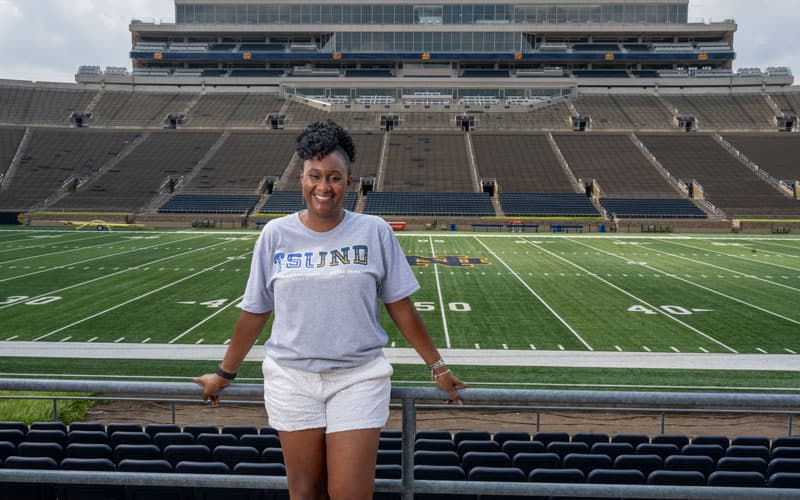 Jennifer Liddell stands inside Notre Dame stadium wearing a shirt that says TSUND.