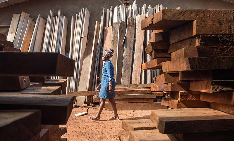 Evelyn Zalwango walks by stacked wood.