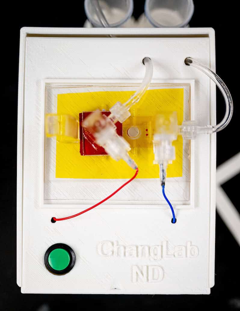 A white plastic box with a yellow and red square and a green button. Cords come out of it. ChangLab ND is imprinted on it.