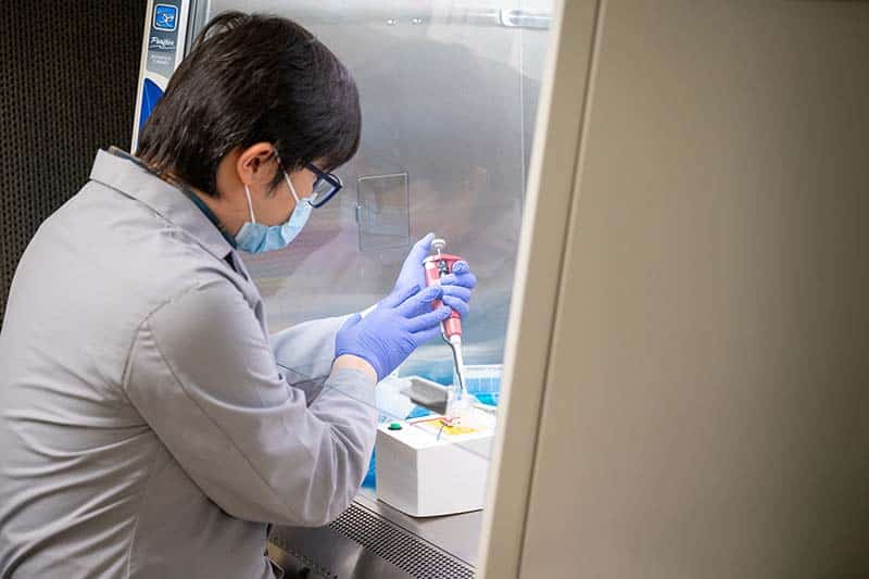 A man in a labcoat works on a COVID-19 test device.