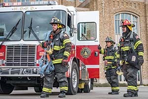 Firefighters in gear walk around a fire truck.