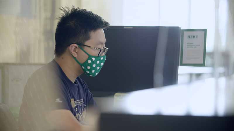 A student on a computer wearing a shamrock patterned, green face mask.