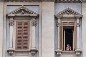 Two large windows in Rome, one with a woman looking out.