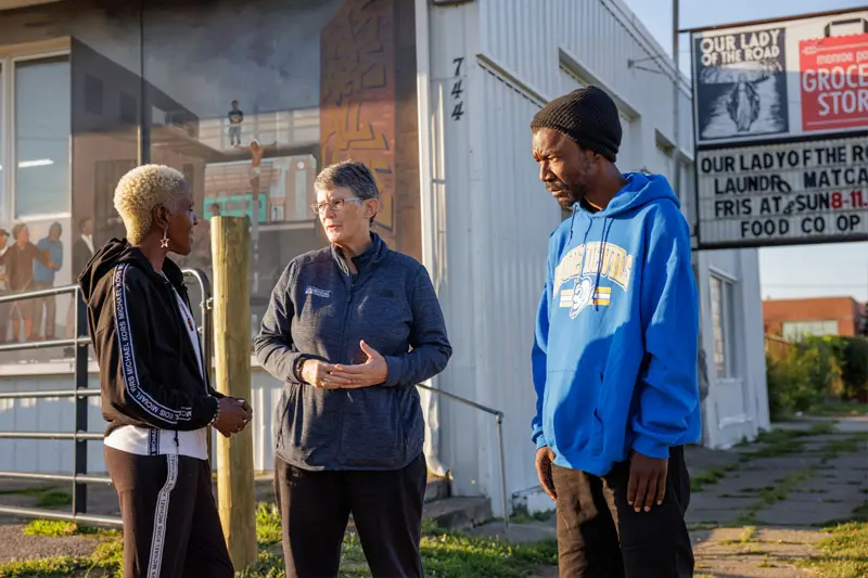 Margie Pfeil stands with two black people talking in front of the Our Lady of the Road day center.